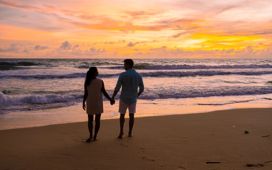 A couple holding hands on the beach at sunset